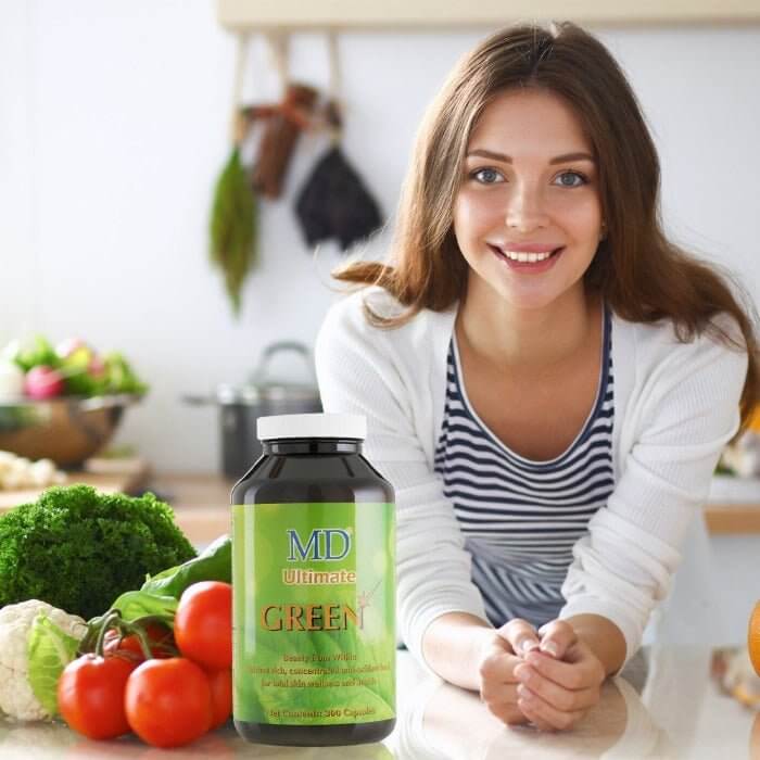 Healthy young woman with fresh vegetables and MD Ultimate Green supplement in kitchen, promoting beauty from within and wellness