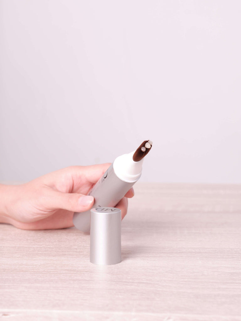Hand holding MD Follicle Energizer from MD Hair collection with clear serum visible on precision brush tip, highlighting light texture and easy scalp application.

